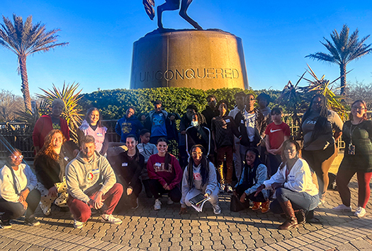 "CSW Arts & Athletic 2022 campers and mentors posing together in front of the Unconquered statue."