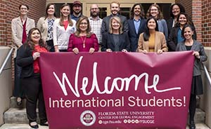 "Center for Global Engagement staff standing on stairs holding an Welcome International Students banner""