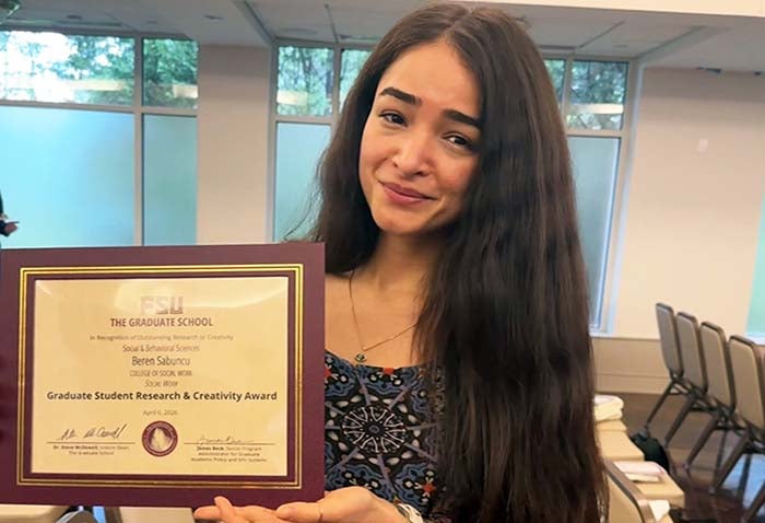 Doctoral student Beren Crim Sabuncu holding her paper certificate for her 2026 Florida State University Doctoral Student Research and Creativity Award.