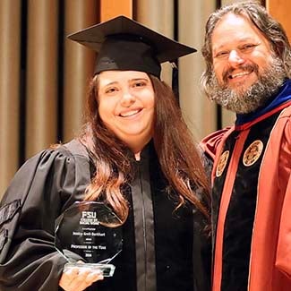 "2026 Professor of the Year Jessica Greil-Burkhart holding her octagonal crystal award posing with Dean David Springer in graduation regalia"