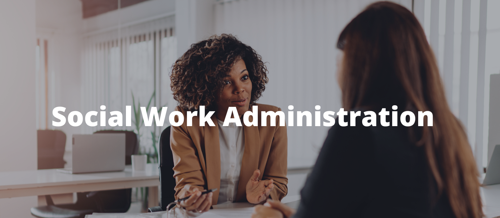 "A person in a tan blazer gestures with hands while speaking to another person across a table in an office setting."