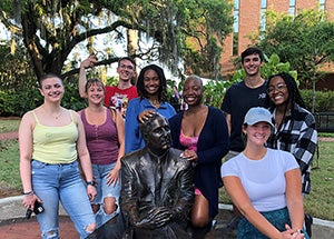 FSU Students posing in front of Westcott building on the Florida State campus with a bronze statue.