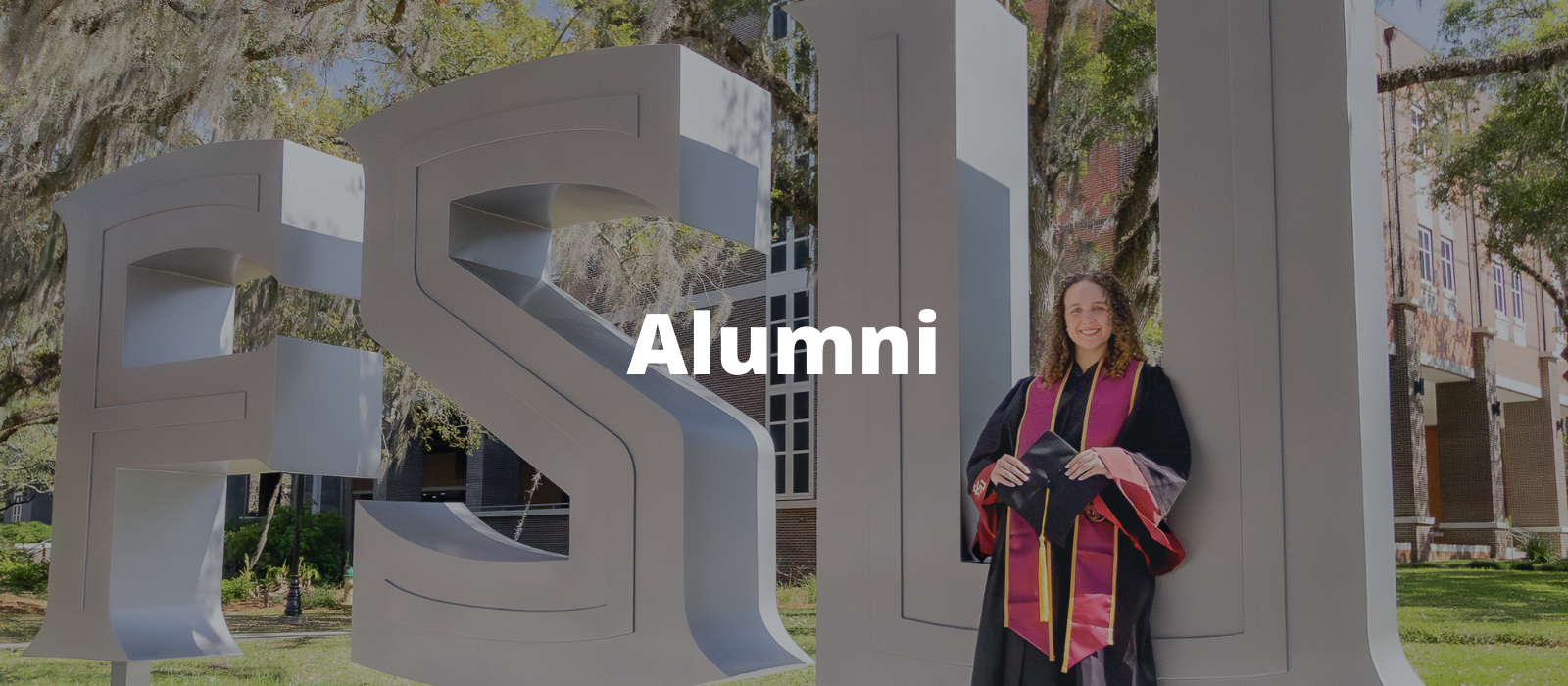 "Alumni header image of the large FSU metal sign with a graduate in regalia posing in front of it"