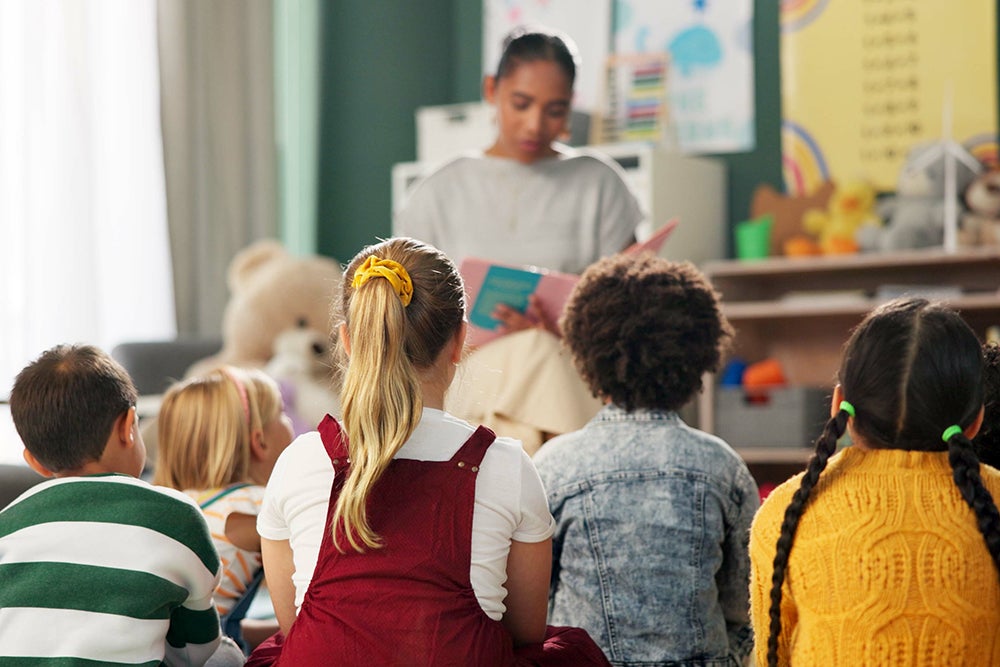 "Adobe stock photo of a woman reading a book to young children seated around her in a classroom setting"