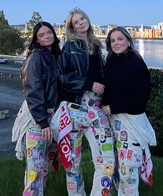 "Beatrice Pap pictured right with two friends wearing white overalls with bright patches on them at Jonkoping University."