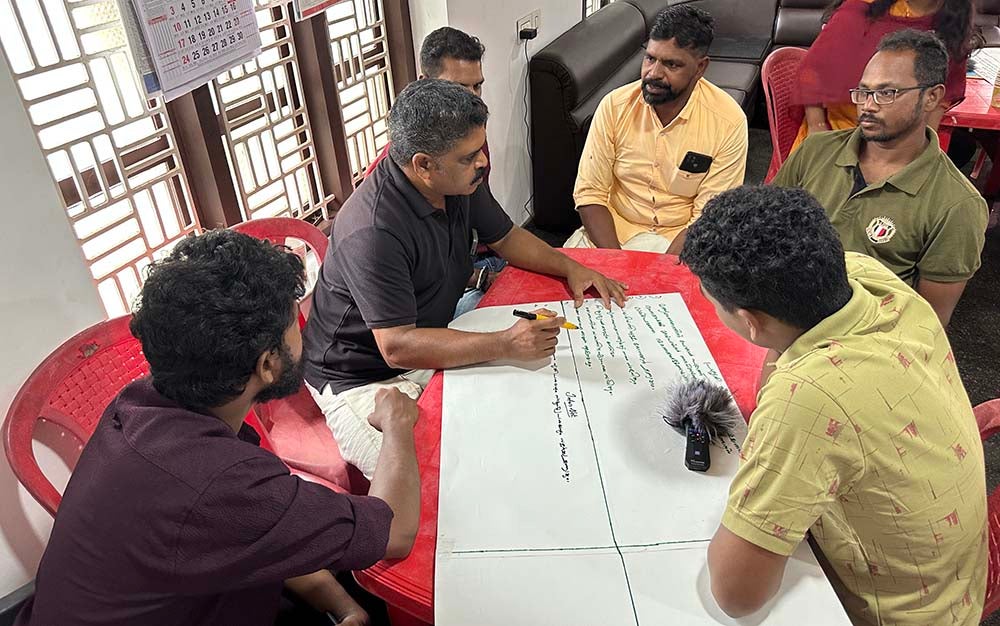 "Kerala residents gathered around a table with a large paper they are writing on during a workshop session"