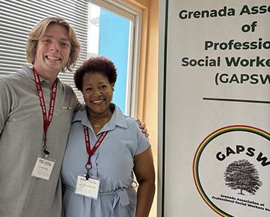 "Connor Davis and Dr. Carol Edwards posing with the Grenada Association of Professional Social Works, Inc. sign""