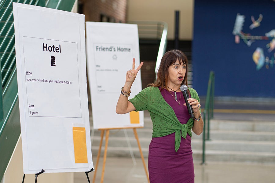 Krista Del Gallo, a facilitator for the “In Their Shoes” simulation, stands with posters used to represent real-life scenarios experienced by domestic violence survivors.