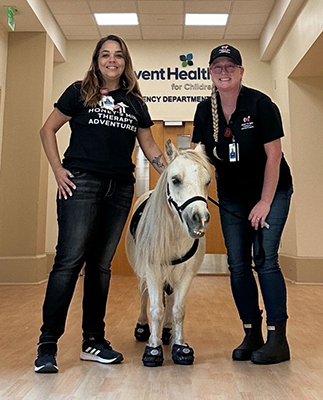 "Fabiana Rocha and Mary Rose Gullet with a white miniature horse at AdventHealth"