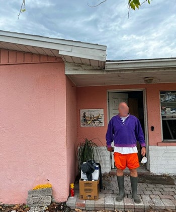 "A man with his face blurred out standing in the open doorway of a pink house"
