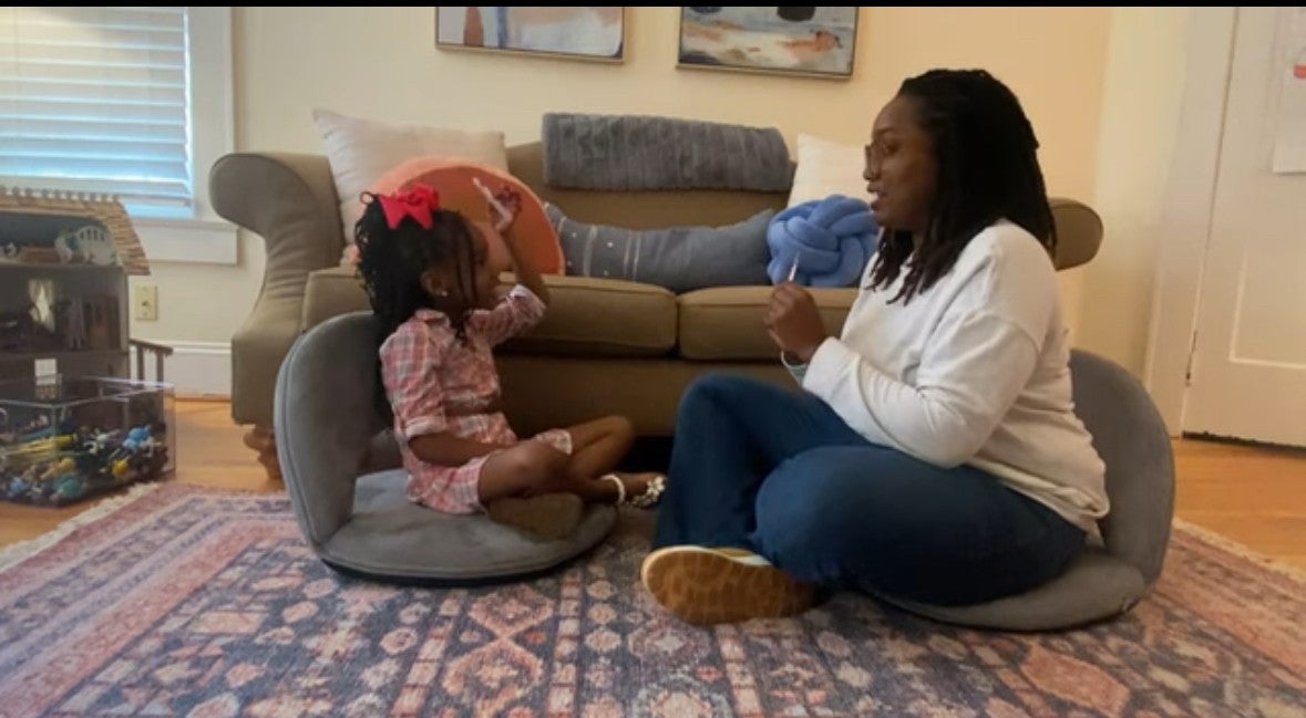 "Photo of Adult sitting on a rug with a little girl playing a game."