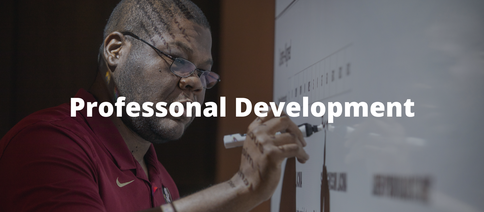 "Man with glasses in an FSU shirt writing on a white board"