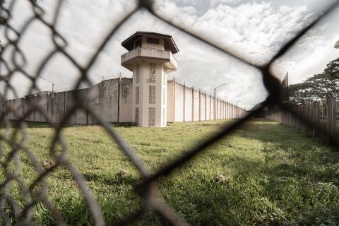Image of the front of a jail watch tower through a chain link fence.
