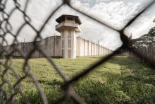 Image of the front of a jail watch tower through a chain link fence.