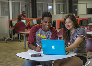 "Photo of students wearing Florida State University clothing sitting at a table looking at a computer in the Academic Center for Excellence computer lab "
