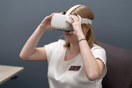 Women with virtual reality goggles on her head. She is holding the goggles with her hands.